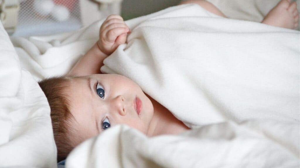 青い目の赤ちゃんが白い毛布に包まっている。