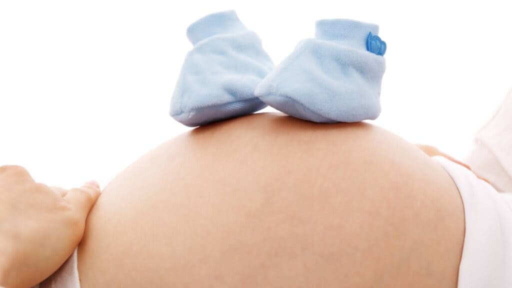 妊娠した大きなおなかの上に赤ちゃんの青い靴下を乗せている