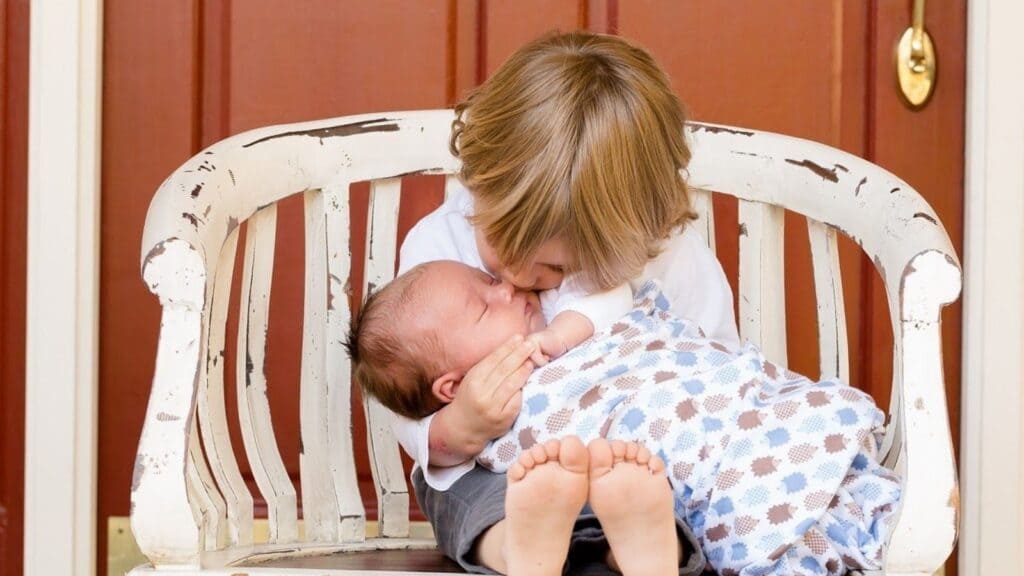 椅子に座ってお姉ちゃんが膝の上に赤ちゃんを乗せてキスをしている